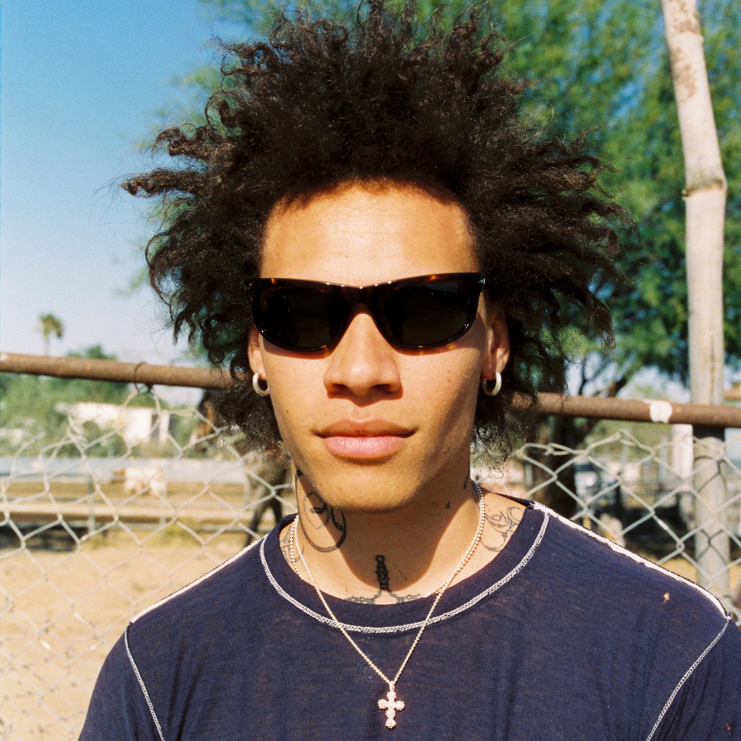 Person wearing sunglasses and a blue t-shirt with a graphic design, standing outdoors. Sad Eyewear Polarized Tortoise Sunglasses