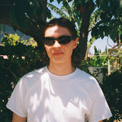 Person wearing sunglasses and a white t-shirt standing in front of green foliage