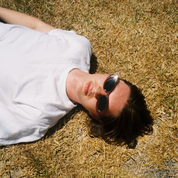 Person lying on dry grass wearing sunglasses and a white shirt