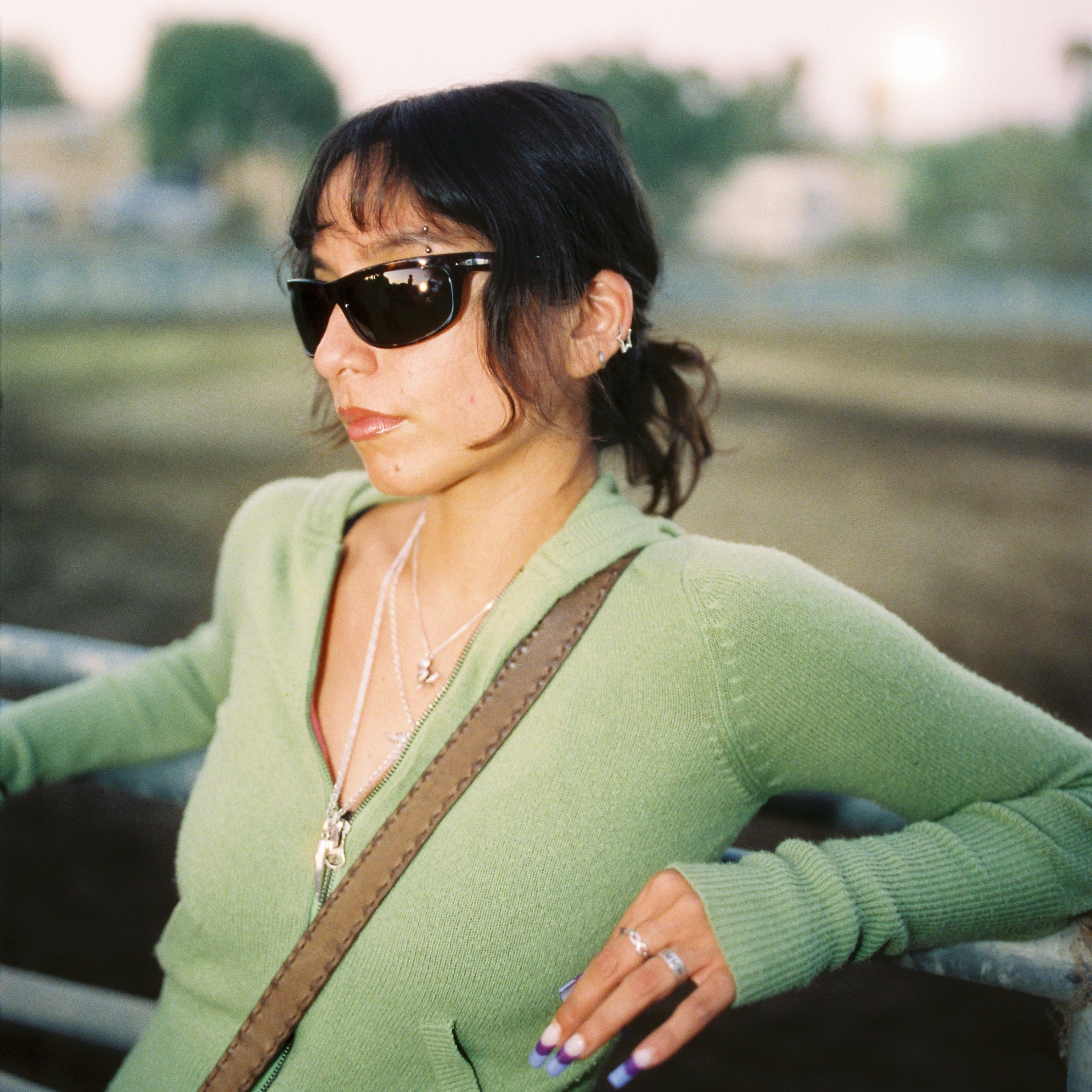 Woman wearing sunglasses and a green sweater with a blurred background
