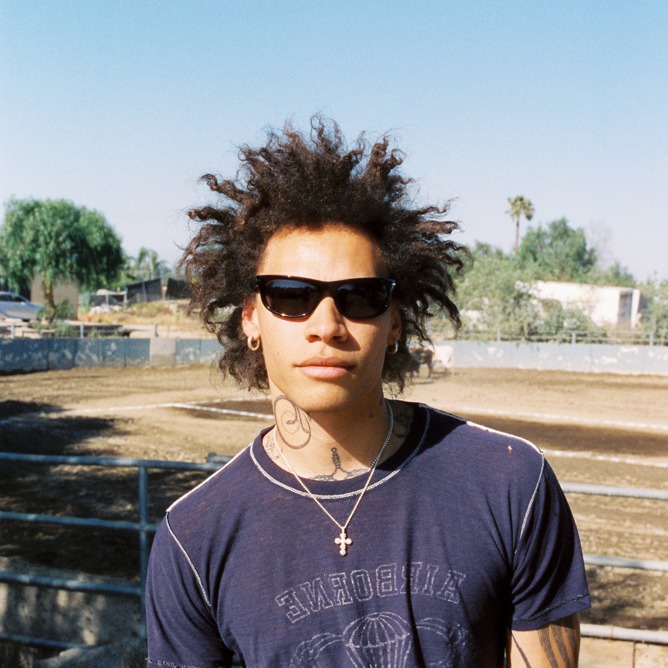 Person wearing sunglasses and a dark t-shirt with a graphic design, standing outdoors.