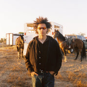 Person standing in a field with horses and a trailer in the background Sad ember Asphalt sunglasses