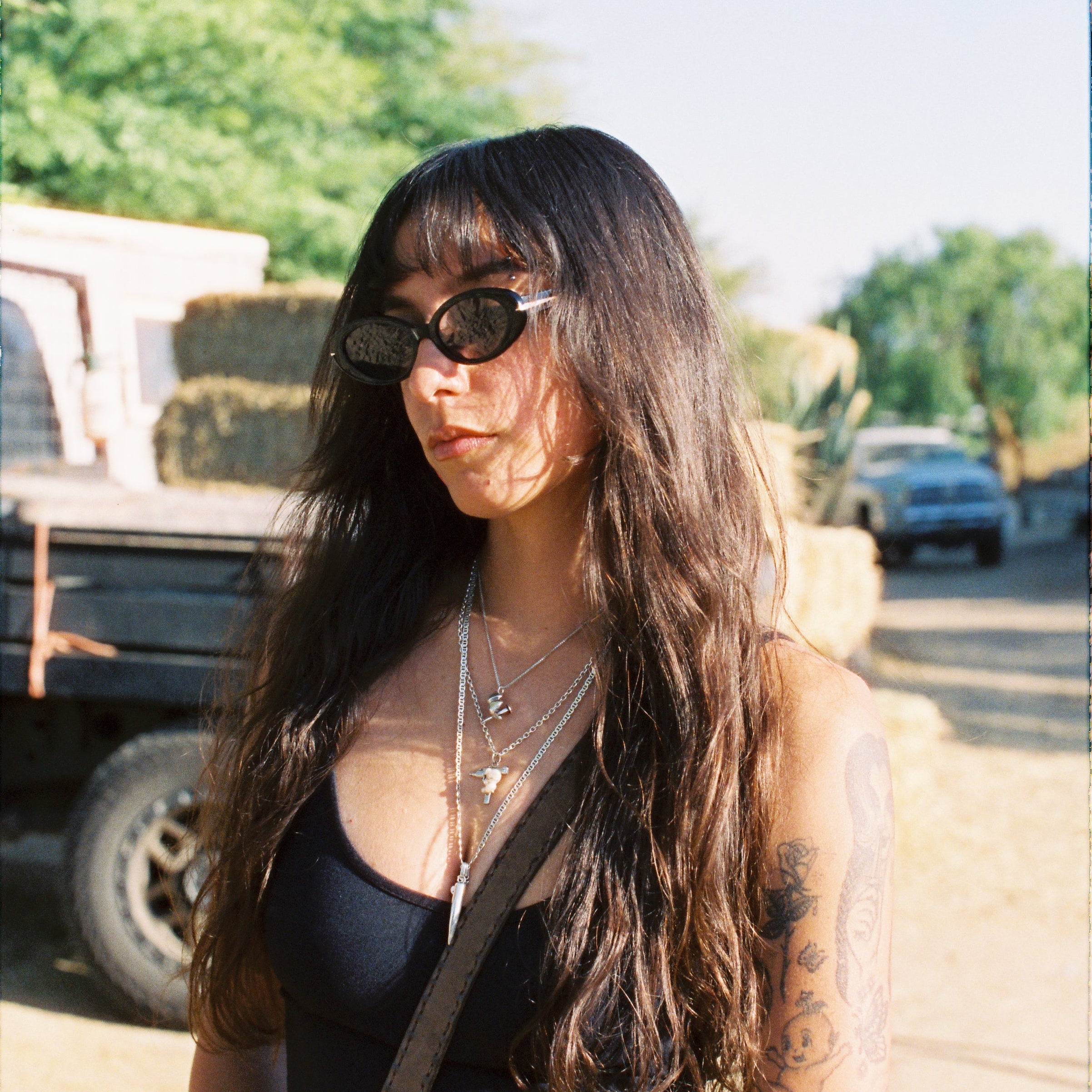 Woman with oval sunglasses and long hair sitting outdoors near a truck