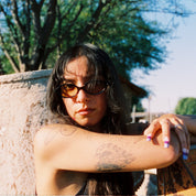 Woman with sunglasses leaning against a large concrete block outdoors